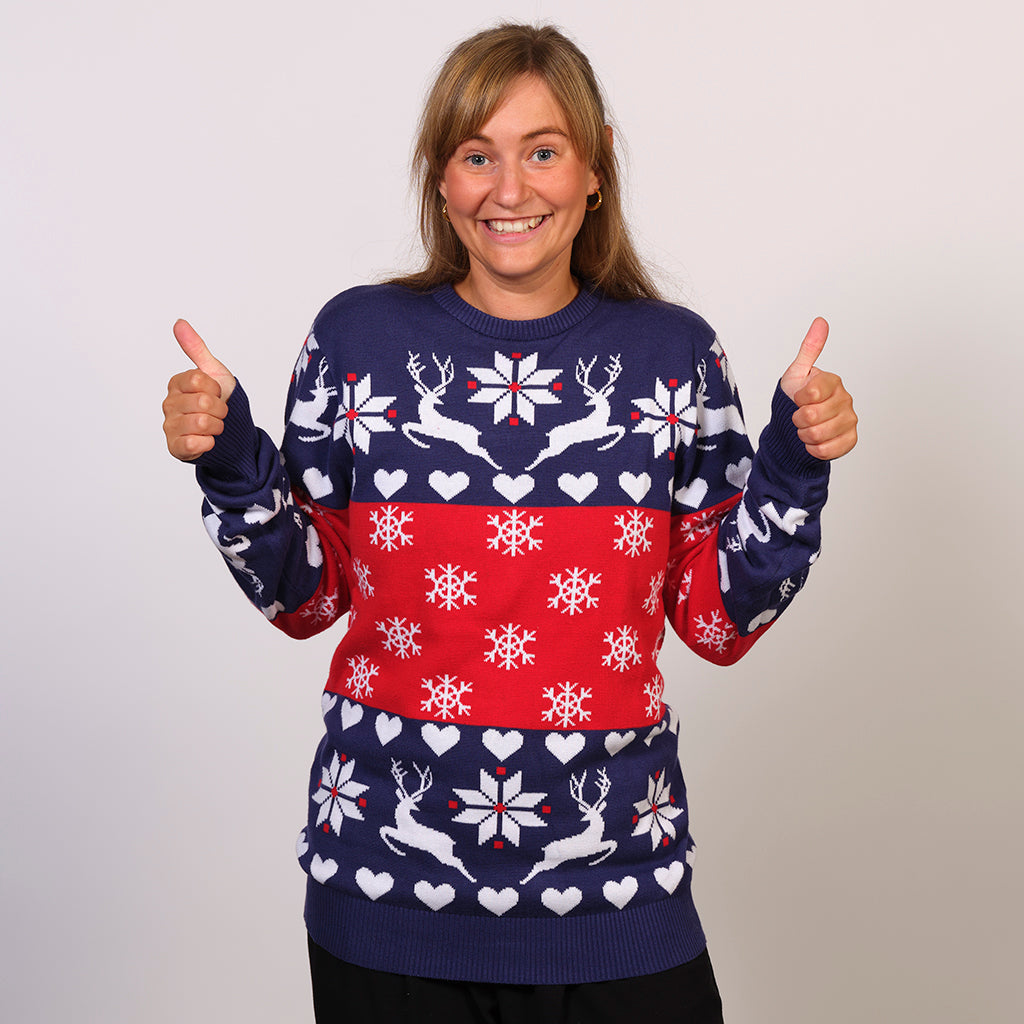En poserende kvinde iført en rød og blå julesweater med snefnug og rensdyr.